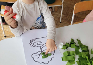 Chłopiec przykleja zielone kulki na koronę drzewa