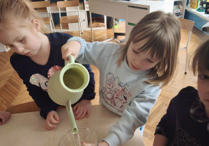 Dziewczynka nalewa wodę konewką do naczynia