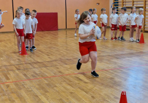 Dziewczynka biegnie z piłka do pachołka