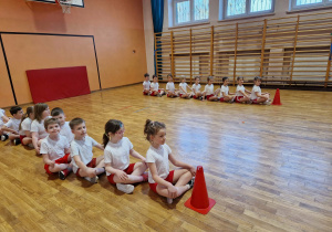Dzieci siedza w siadzie skrzyżnym w dwóch rzędach