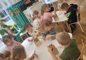 Dzieci siedzą przy stoliku i kolorują ilustrację
