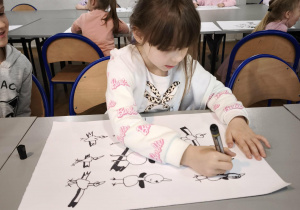 Dziewczynka maluje bociany czarnym flamastrem