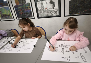 Dziewczynki przy stole rysują bociany na kartonie